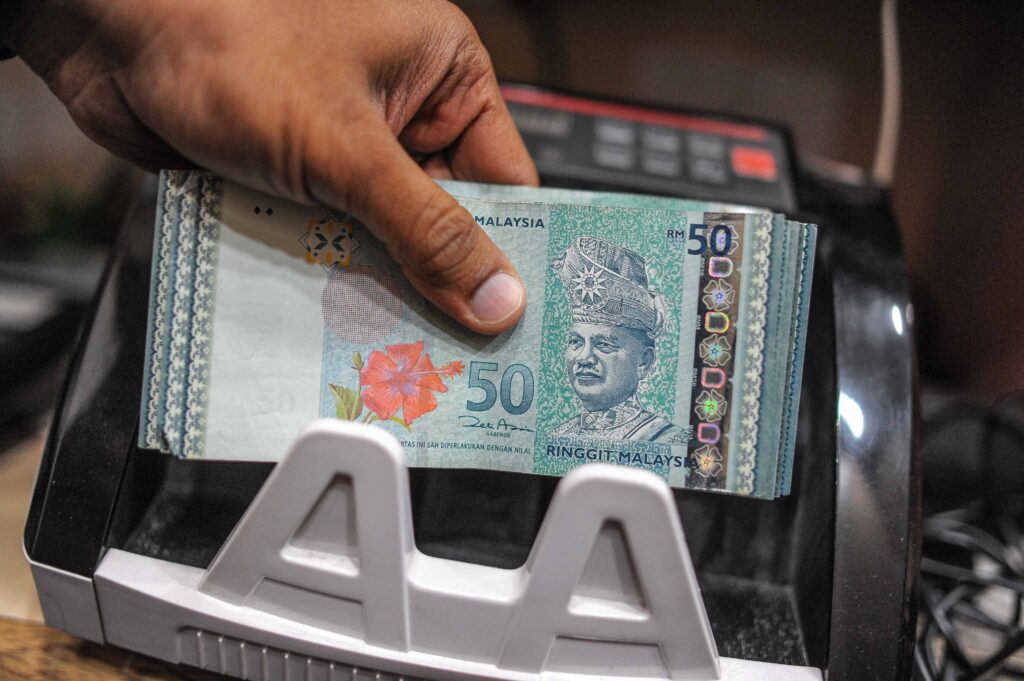 A money changer counts Malaysian ringgit banknotes for customers in Kuala Lumpur