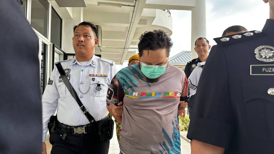 Police officers escort Muhamad Shafiq Salleh at the Segamat magistrate's court ahead of the trial