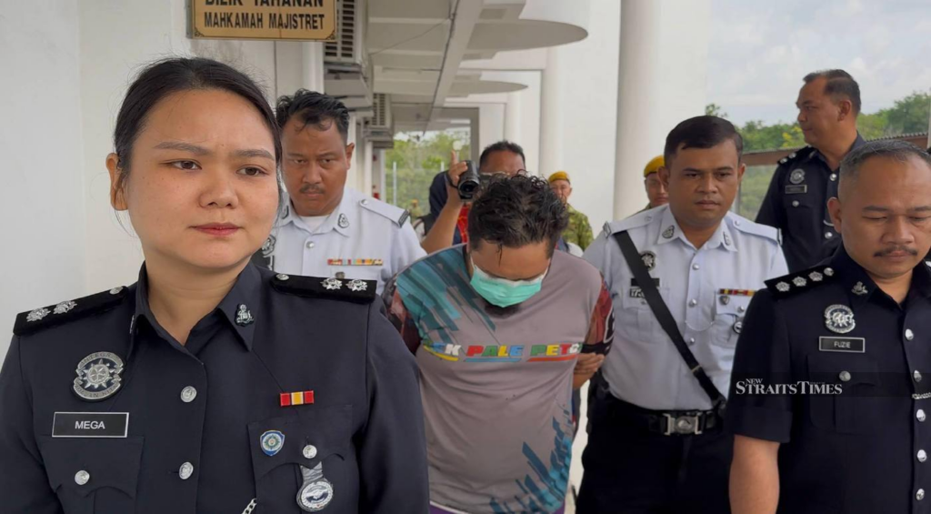 Police officers escort Muhamad Shafiq Salleh at the Segamat magistrate's court ahead of the trial